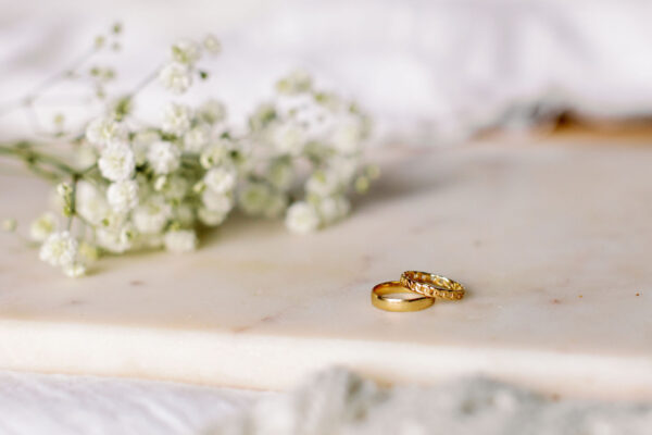 The Other Ellen 14k Gold Cigar Band on a countertop with another ring and flowers